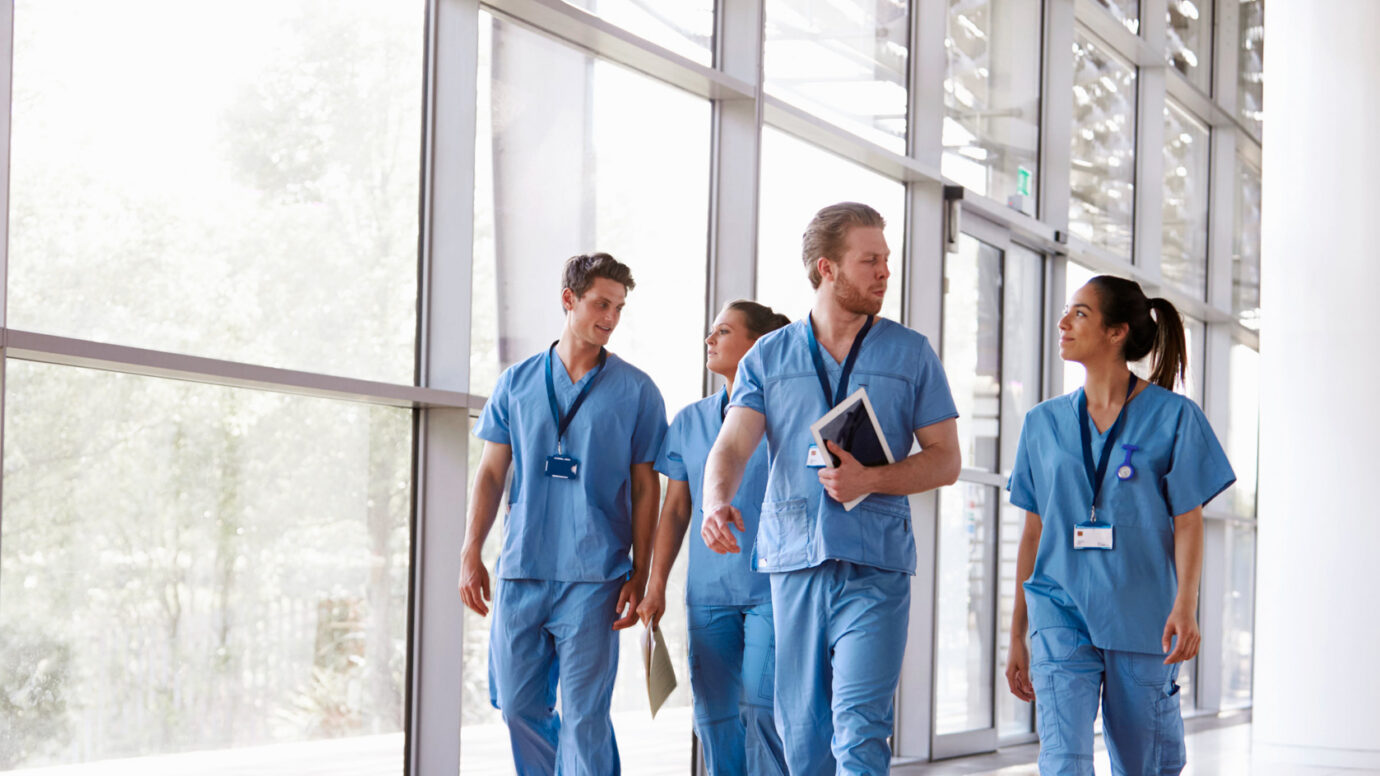 Four healthcare workers in scrubs walking in corridor